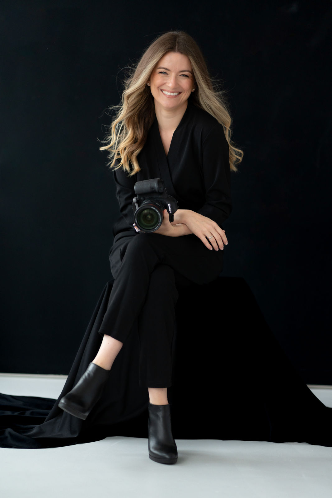 Cate Schmitt Portrait Branding Fotografin Schwangerschaftsfotografie Bamberg | Fotografin in schwarz gekleidet sitzend mit Canon DSLR Kamera im Studio